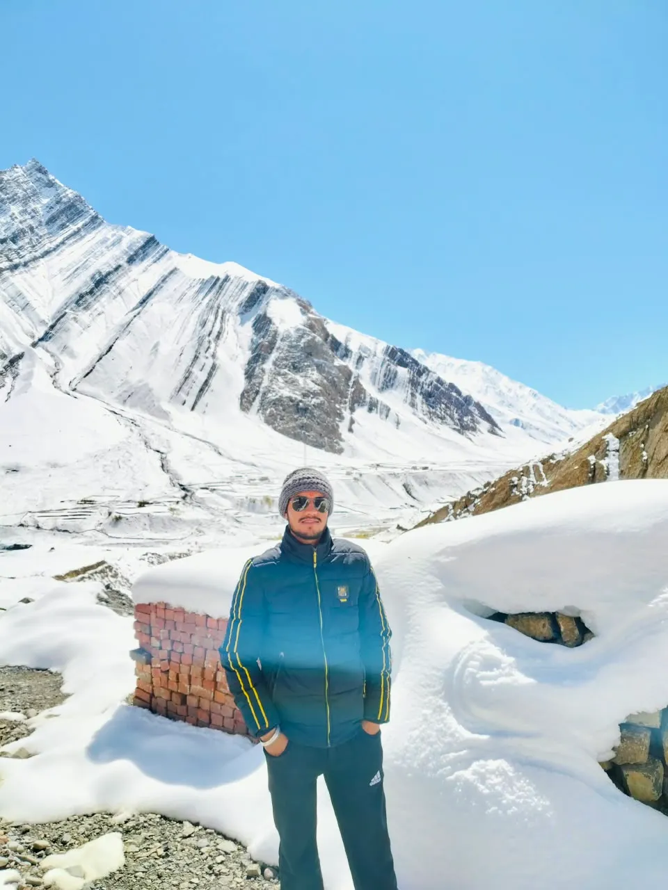 Kulwant in a puffer jacket and wool cap, deep snow around him and a snow-covered valley beyond